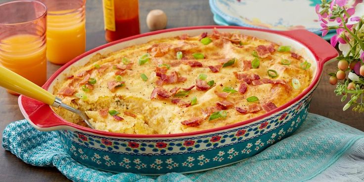 a casserole dish with bacon and green onions in it on a table next to orange juice