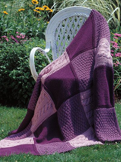 a purple and pink blanket sitting on top of a white chair next to a flower garden