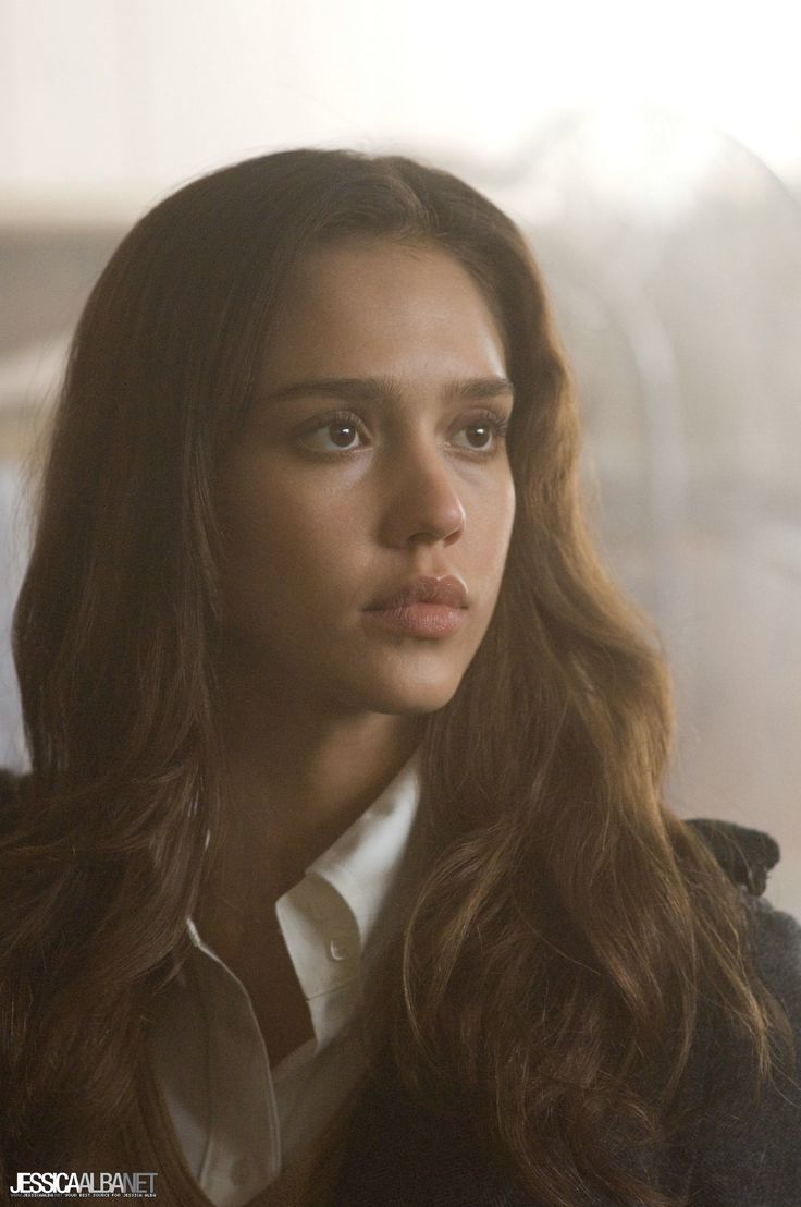 a woman with long brown hair wearing a white shirt and black jacket looking off into the distance