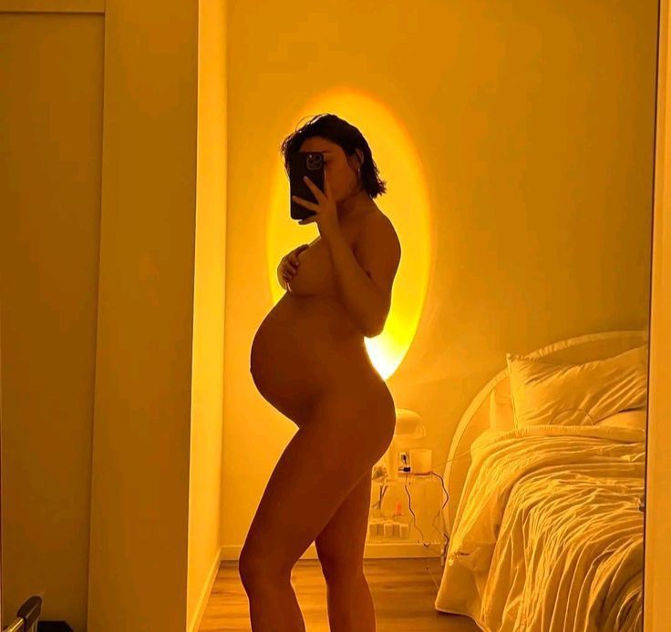 a pregnant woman is taking a selfie in the mirror with her cell phone while standing next to a bed