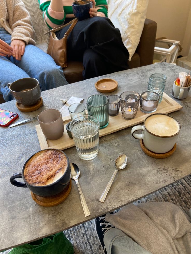 two people sitting at a table with coffee cups and spoons on top of it