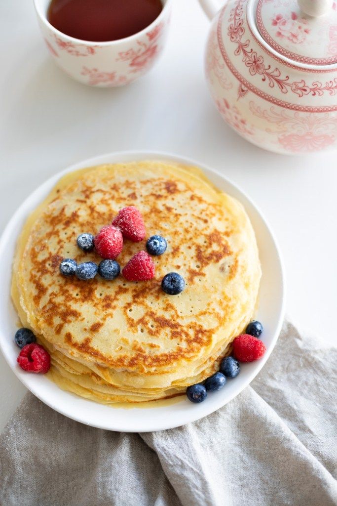 pancakes with berries and blueberries are on a plate next to a cup of tea