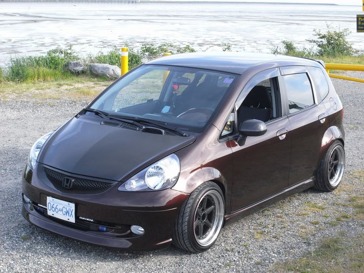 a small brown car parked on top of a gravel road next to a body of water