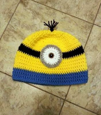 a crocheted yellow and blue hat with an eyeball on the front, sitting on a tile floor