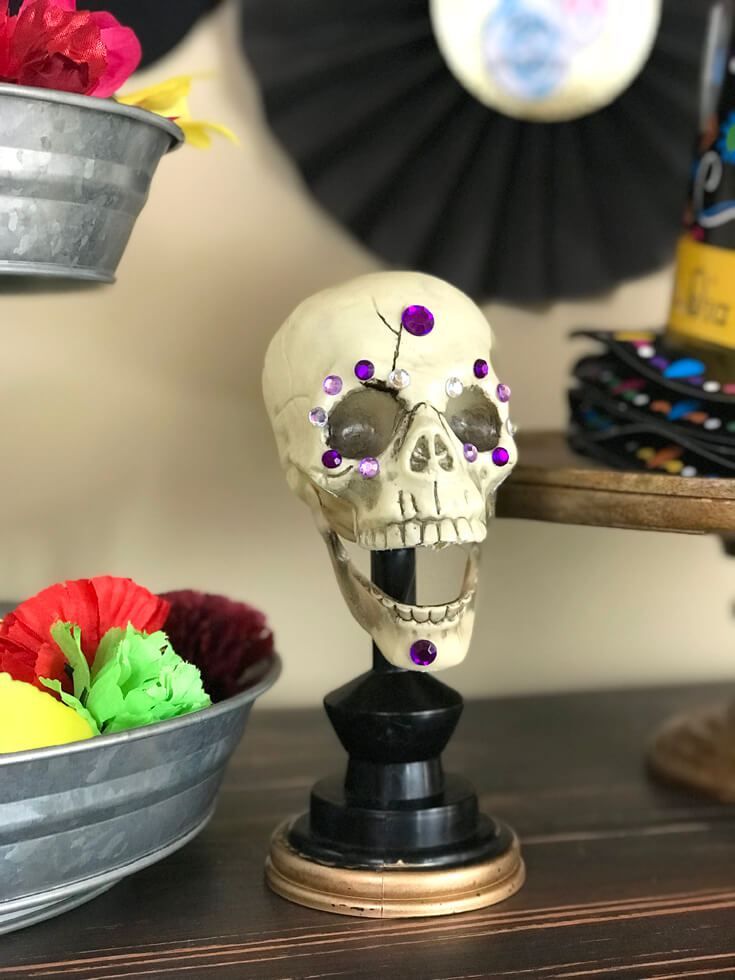 a fake skull sitting on top of a wooden table next to some bowls with flowers