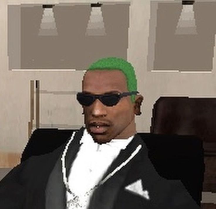 a man with green hair and sunglasses sitting in front of a computer screen wearing a black suit