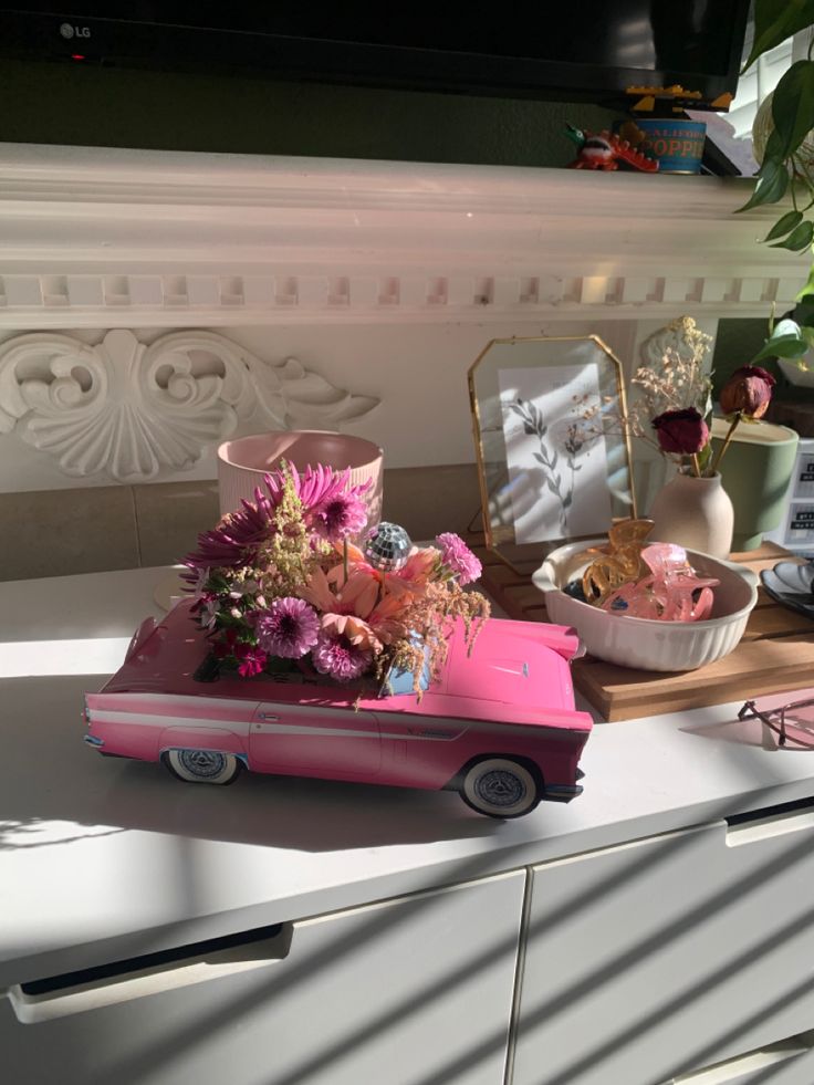 a pink toy car with flowers in it sitting on top of a dresser next to a mirror