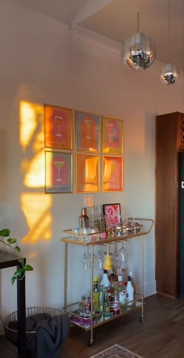 a bar cart in the corner of a room with pictures on the wall behind it