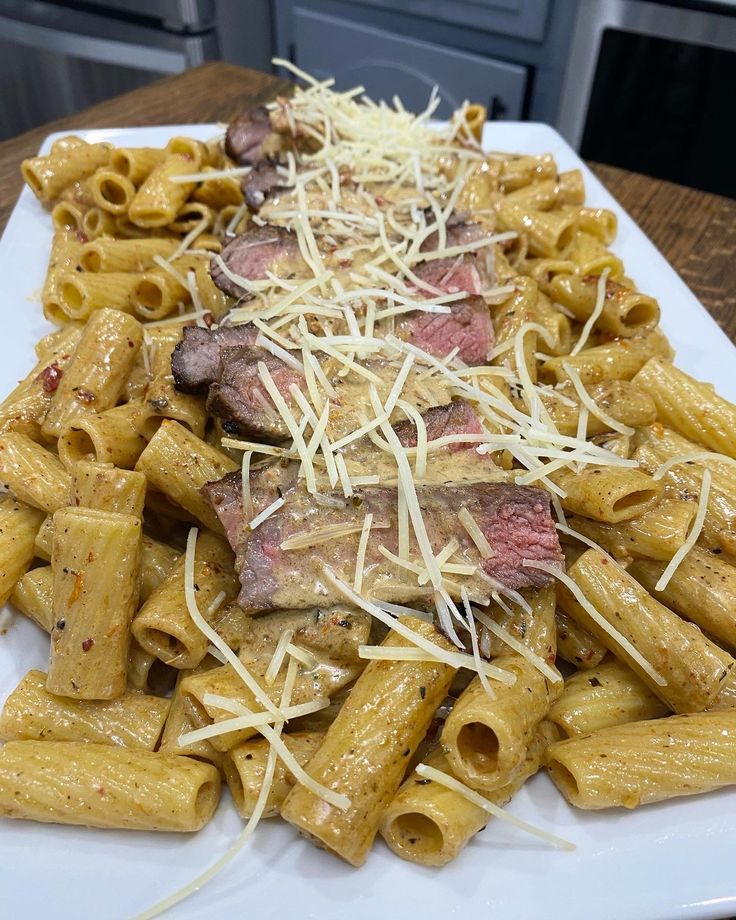 a white plate topped with pasta and meat covered in cheese