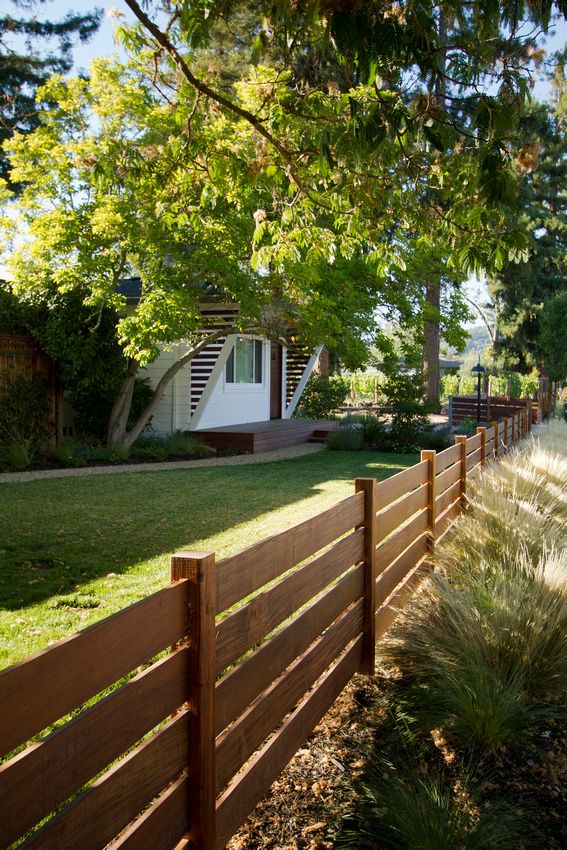 a wooden fence in front of a house with trees and grass on the side walk