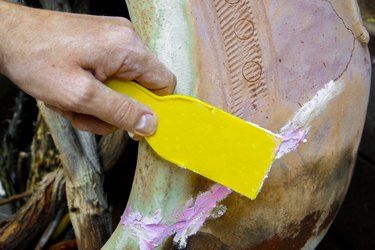 a person using a yellow sponge to paint a vase