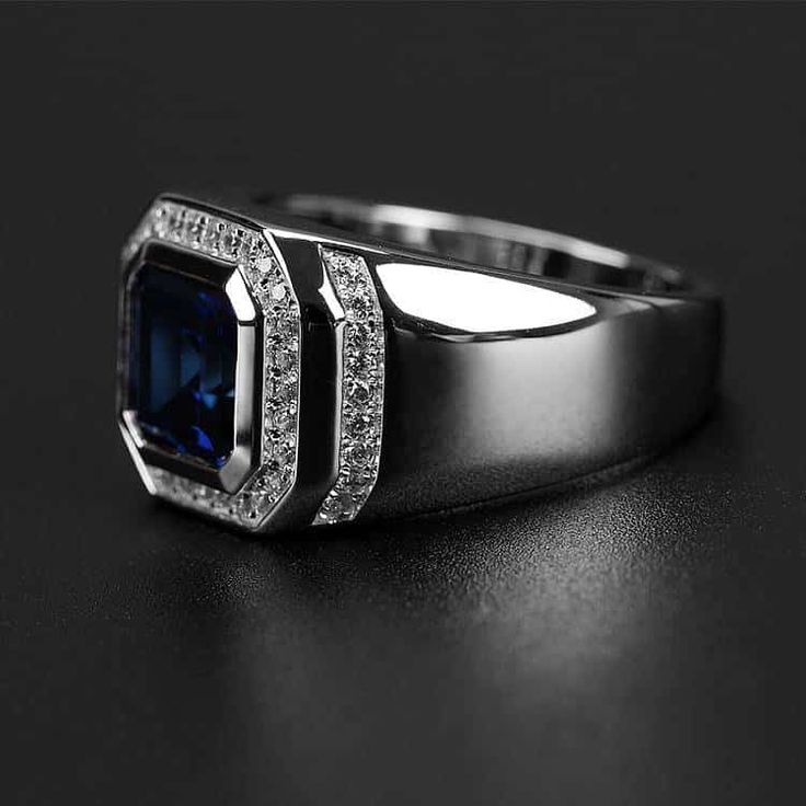 an engagement ring with a blue stone surrounded by white diamonds on a black surface in the dark