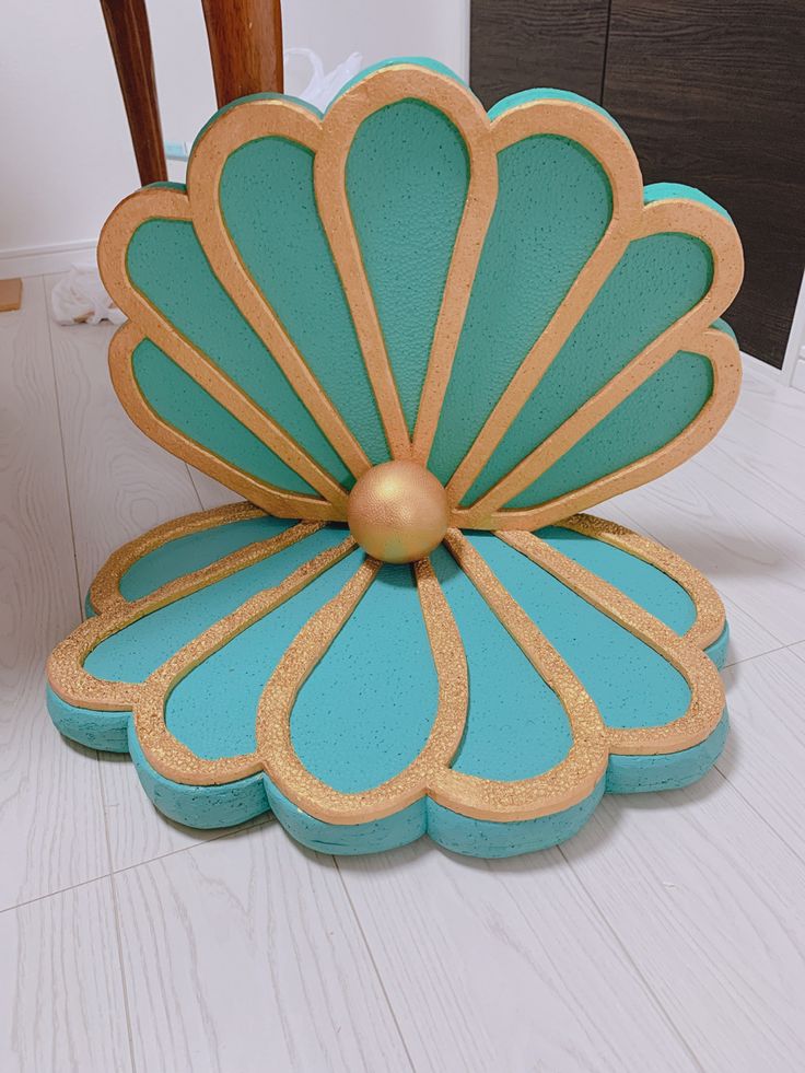 a blue and gold flower shaped object sitting on top of a white floor next to a wooden chair