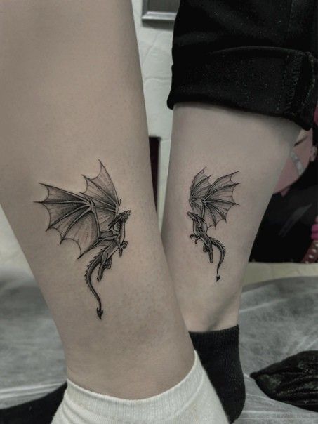 two people with tattoos on their legs, one has a dragon and the other has a bird