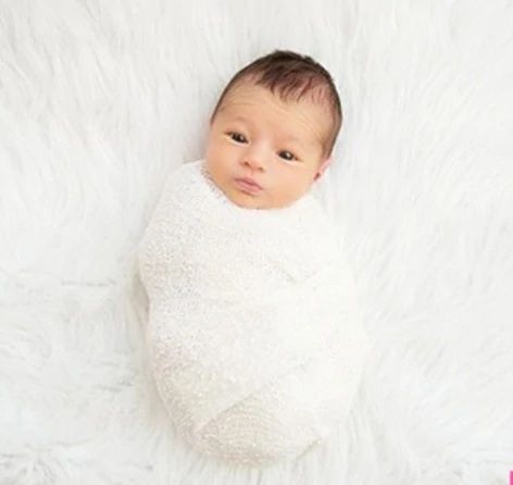 a baby wrapped in a white blanket laying on top of a pink flowered bed