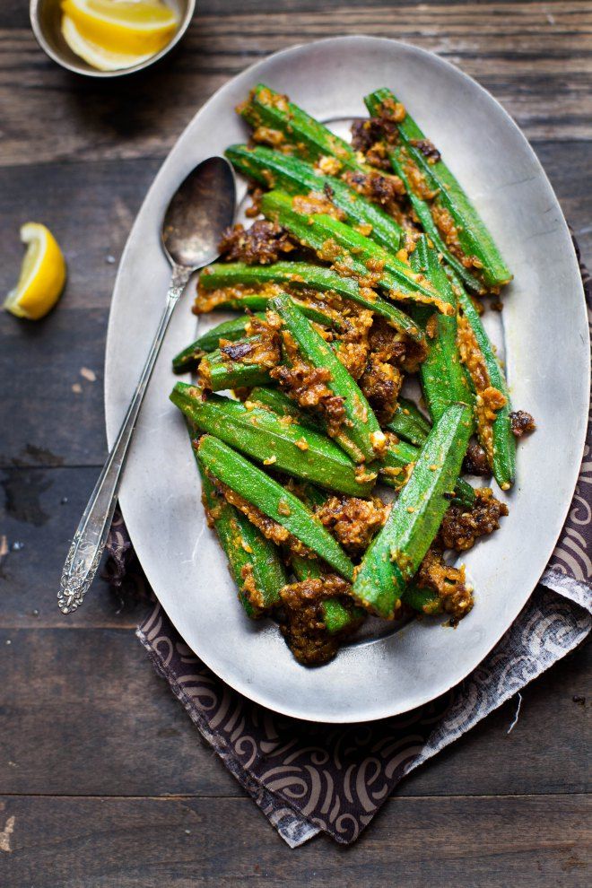 a white plate topped with green beans covered in seasoning next to lemon wedges