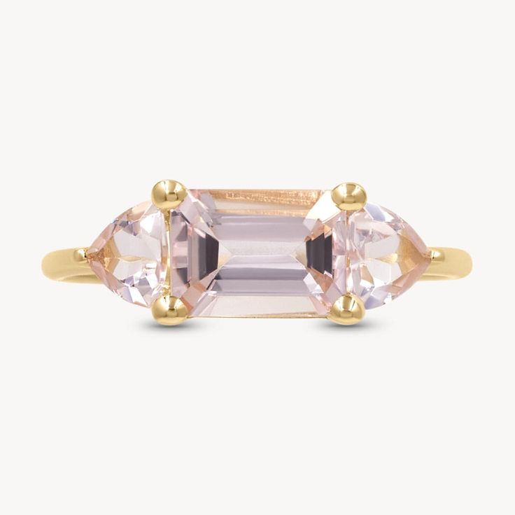 14 Yellow Gold Ring with Natural Morganite. A gem of unparalleled beauty emanates a soft blush hue that exudes both warmth and elegance. Its unique orientation across the finger sets a harmonious tone, inviting admiration from every angle. Flanking this ethereal gem are two majestic trillion-cut morganites with their precisely faceted contours enhancing the ring's overall splendor. Elegant Pink Gold Morganite Rings, Morganite Pink Gold Rings For Formal Occasions, Formal Morganite Rings In Pink Gold, Elegant Morganite Diamond Ring With Gemstone, Formal Morganite Pink Gold Rings, Formal Pink Gold Morganite Rings, Elegant Morganite Rings With Baguette Cut, Morganite Pink Gold Rings With Accent Stones, Pink Gold Morganite Rings With Accent Stones