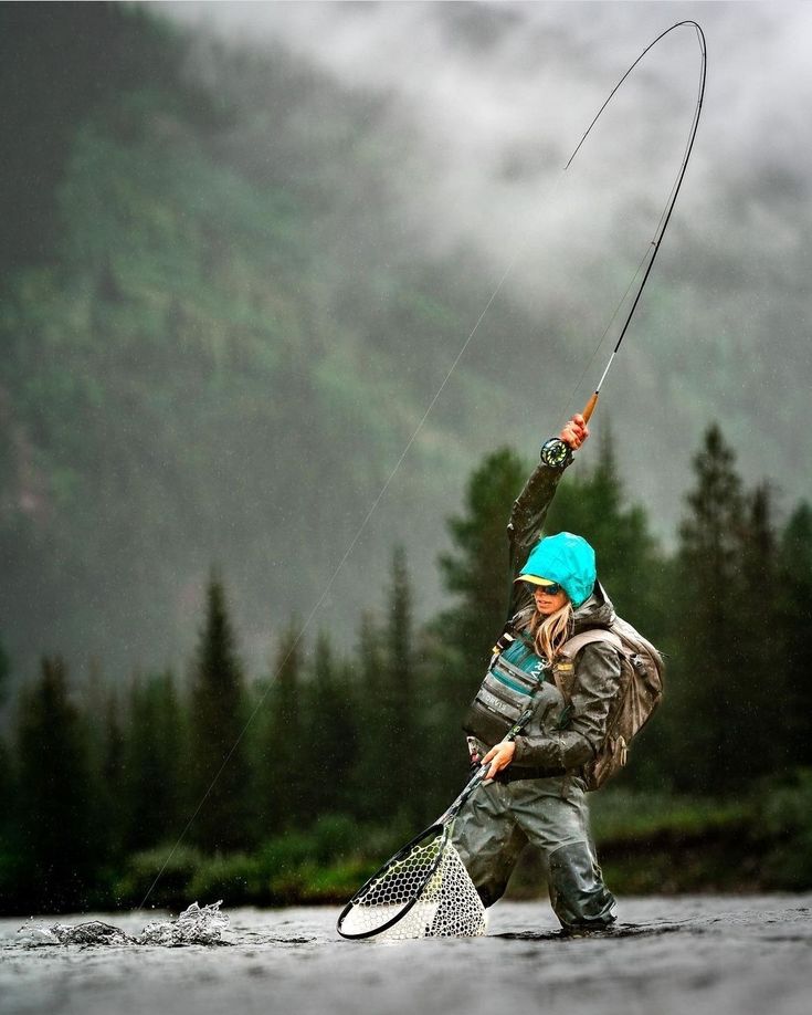 a woman holding a fishing rod and wearing a blue hat while standing in the water