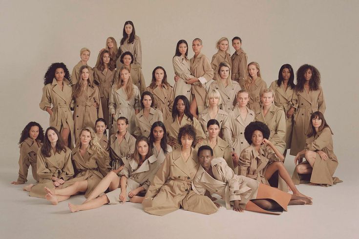 a group of young women in trench coats posing for a photo with one woman sitting on the floor