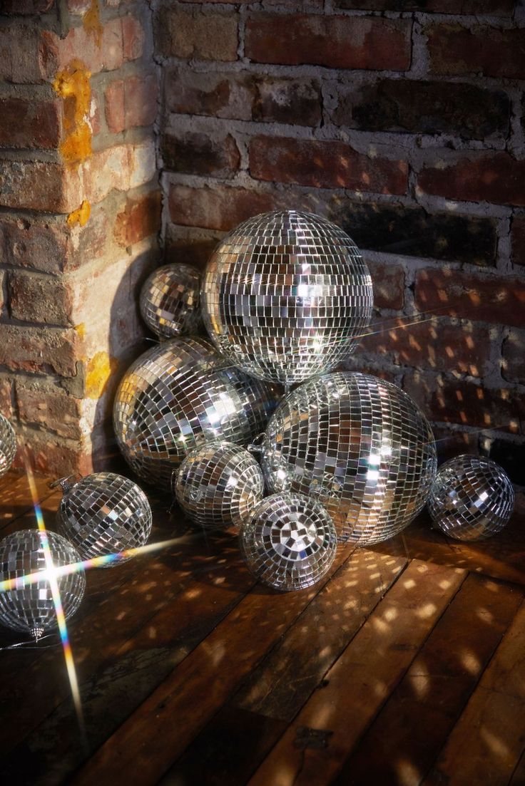 several shiny disco balls sitting on top of a wooden floor next to a brick wall