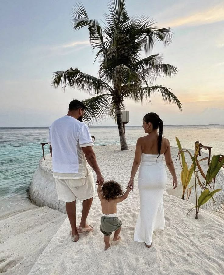 a man and woman holding hands while walking on the beach with a small child in front of them