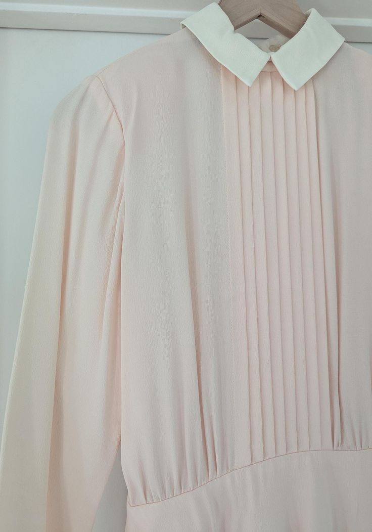 1980s baby pink dress  with contrast white collar Made by Bill Geoffreys Size: 4 Care: Dry Clean Only Details: Contrast White collar  that can be held together with a hook and eye or left open 8 pleated at the center front that start at the neckline to the waistband gathering where the bodice meets the waistband  Pleated skirt The closure is on the center back with 10 button ( last 3 buttons on the waistband ) Elegant Pink Doll Collar Dress, Classic Pink Long Sleeve Dress, Elegant Pink Collared Dress, Pink Pleated Dress For Work, Feminine Pink Dress With Peter Pan Collar, Pink Peter Pan Collar Dress For Spring, Pink Spring Dress With Peter Pan Collar, Pink Retro Dress With Peter Pan Collar, Retro Pink Collared Dress