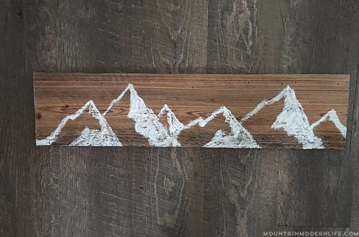 a wooden sign with white mountains painted on it's sides and wood planks