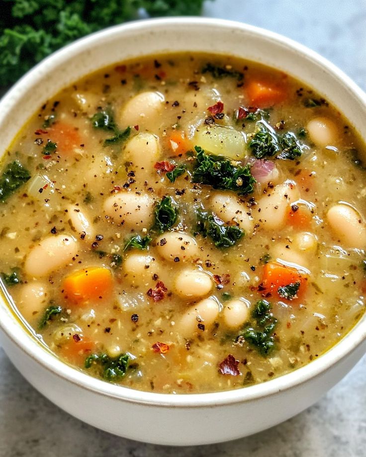 a white bowl filled with bean and vegetable soup on top of a marble countertop