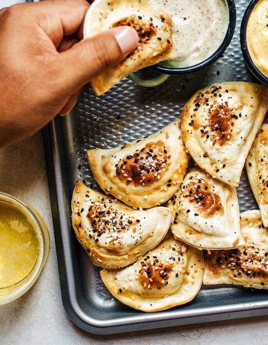 a tray with some pita breads and dipping sauce on the side, along with two bowls of dip