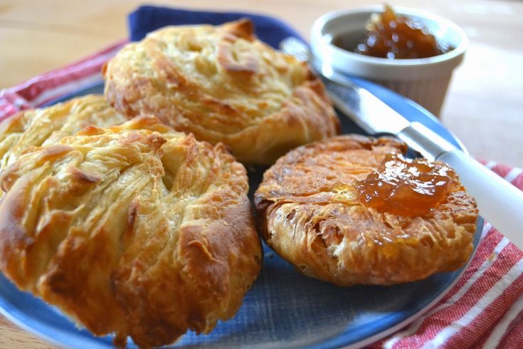 three baked pastries on a blue plate next to a bowl of jam