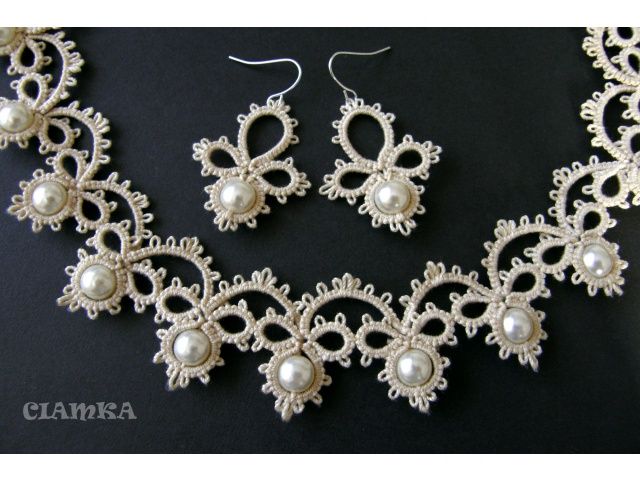 a necklace and earring set made out of white lace with pearls on the sides