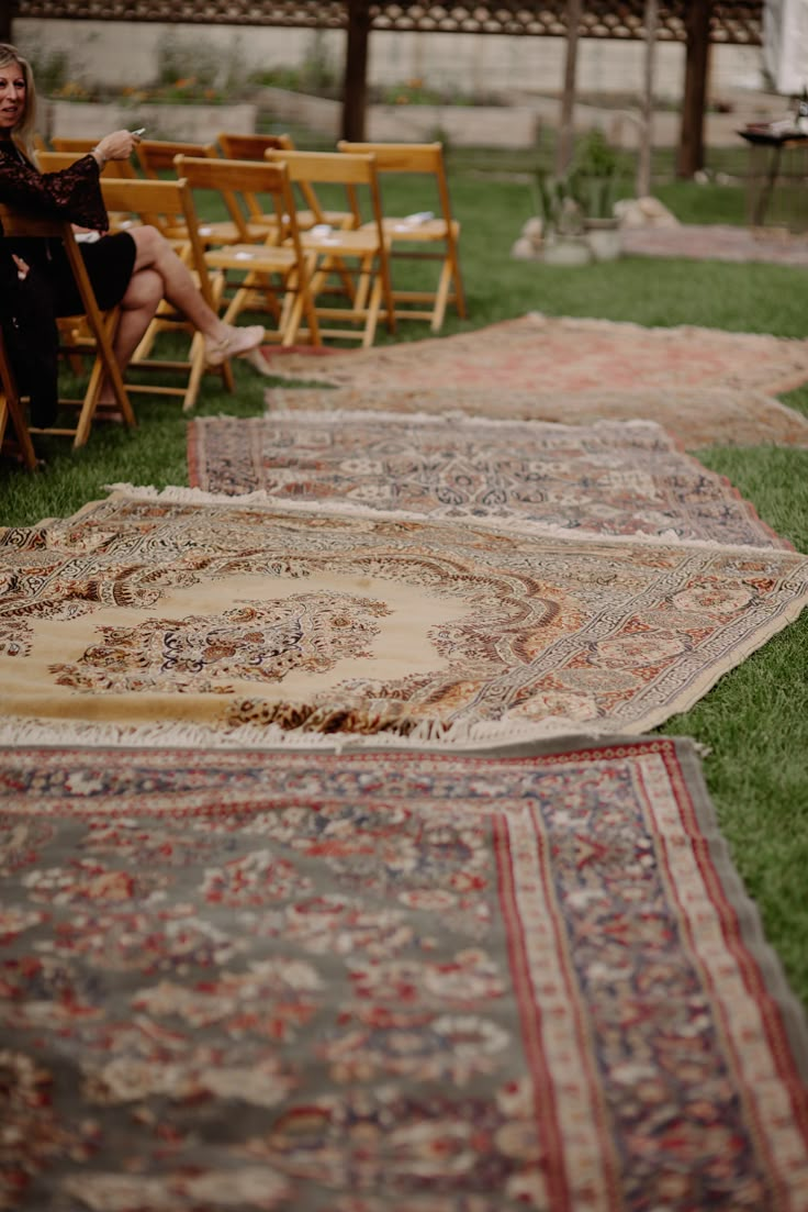 several rugs are laid out on the grass in front of people sitting at chairs