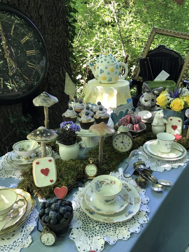 a table topped with lots of different types of dishes and cupcakes next to a clock