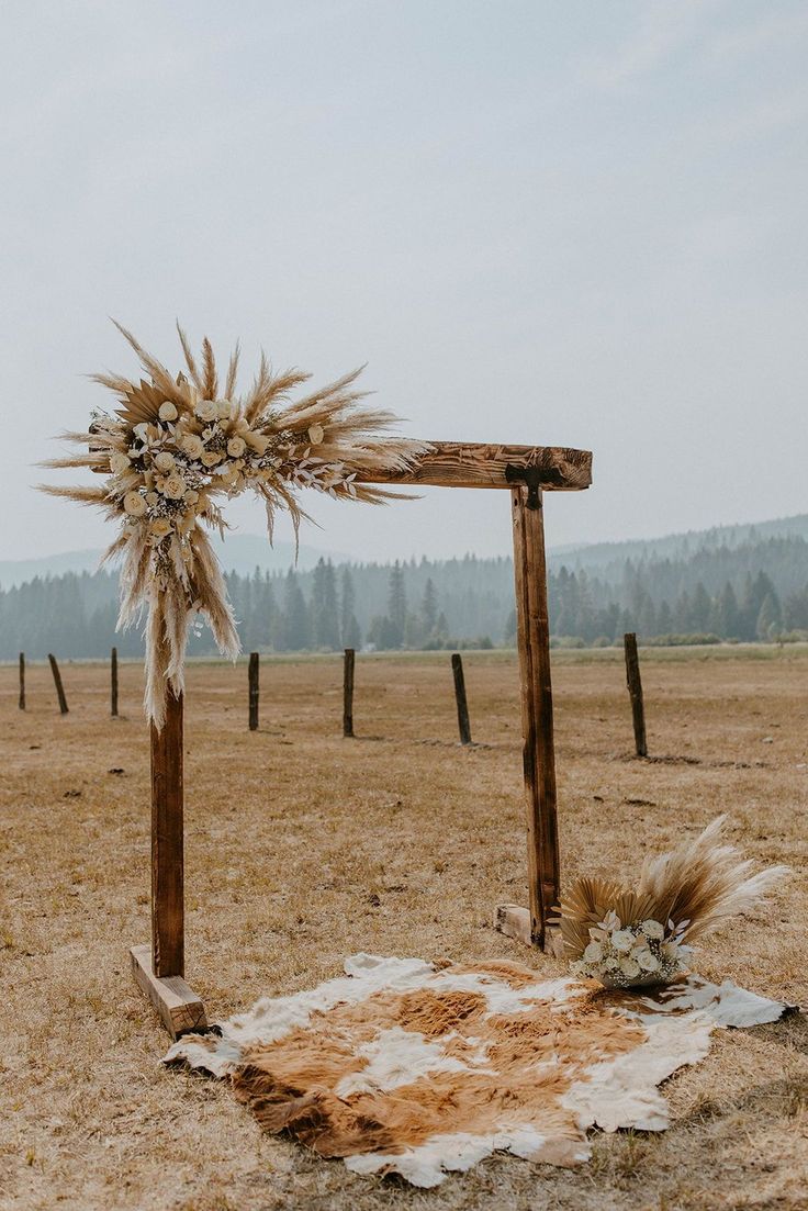 an old wooden structure with dried flowers on it in the middle of a grassy field