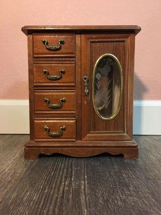 a wooden cabinet with drawers and a mirror on the front door, against a pink wall