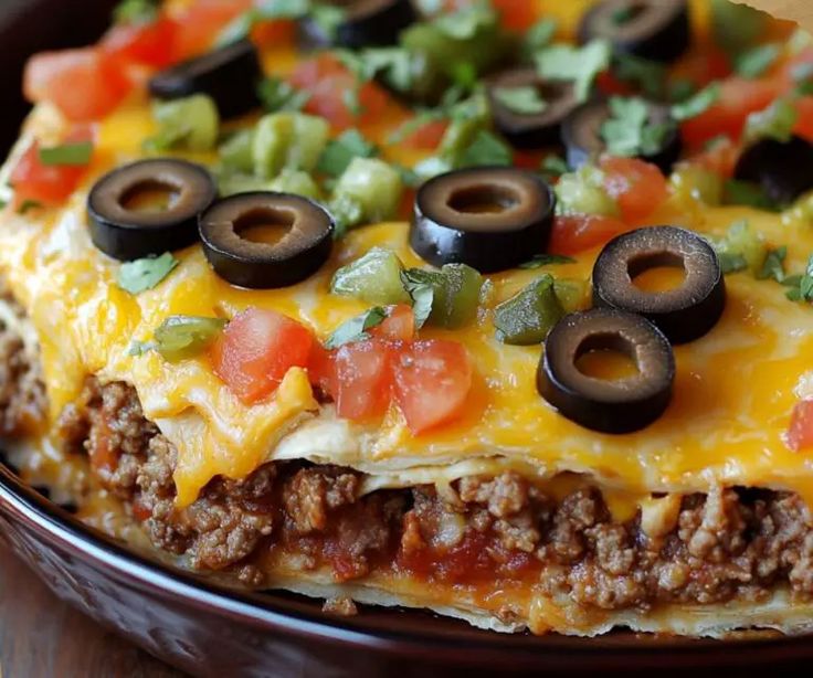 an enchilada dish with black olives, tomatoes, and peppers on it