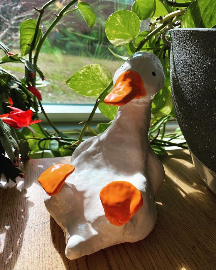 a ceramic duck sitting on top of a wooden table next to a potted plant