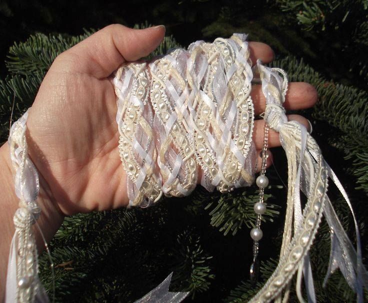 a hand is holding some white ribbon and beaded bracelets in front of a pine tree