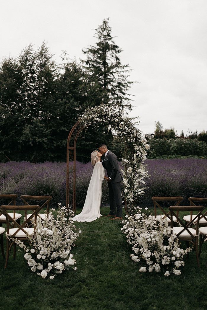 a bride and groom standing in front of an arch decorated with white flowers at their wedding ceremony