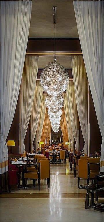 an elegant dining room with chandelier and white drapes on the ceiling, along with yellow chairs