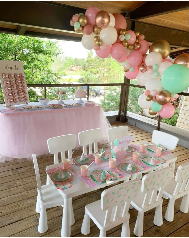 a table set up for a party with pink, white and gold balloons hanging from the ceiling