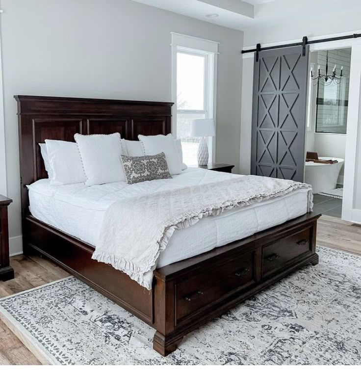 a large bed with white sheets and pillows in a bedroom next to a door that leads to a bathroom