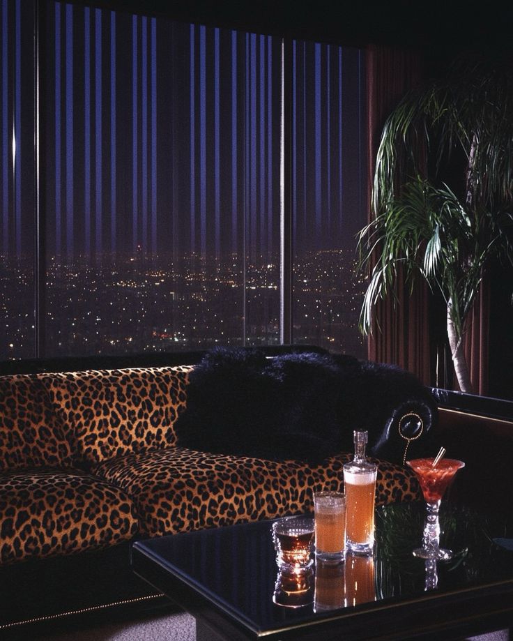 a leopard print couch in front of a large window with city lights and palm trees