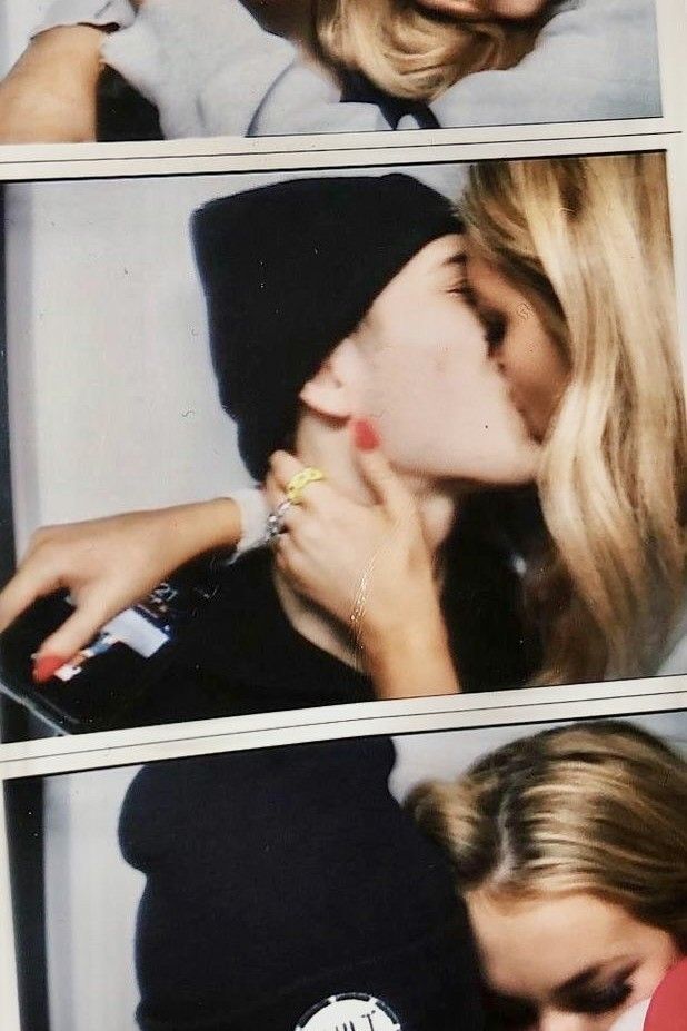 two women kissing each other while wearing beanies and holding onto one another's finger