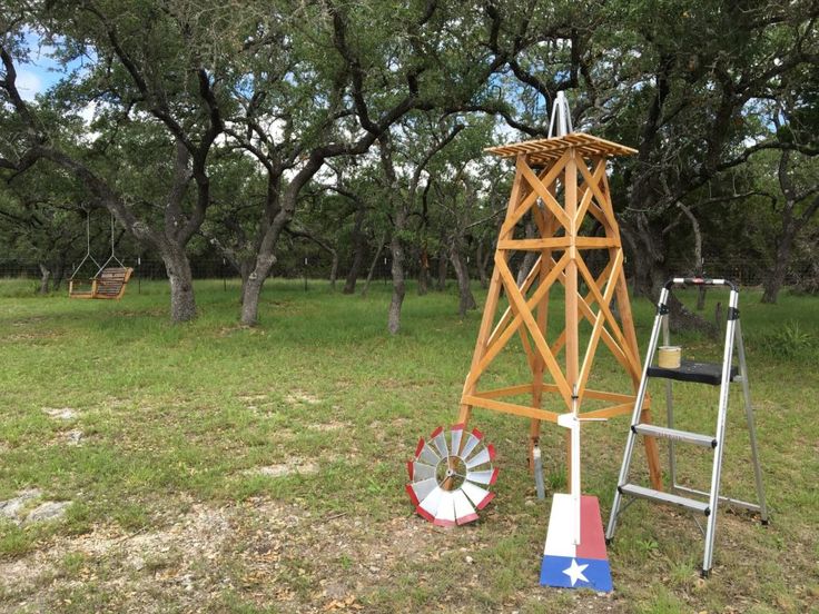 a small wooden structure in the middle of a grassy area with trees and ladders