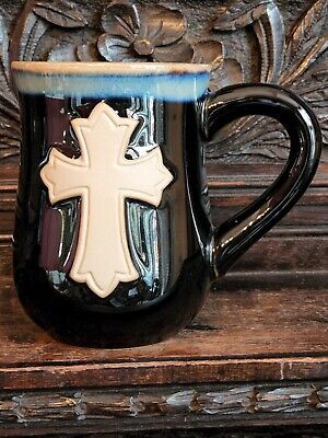 a black and white coffee mug with a cross on the side, sitting on a wooden table