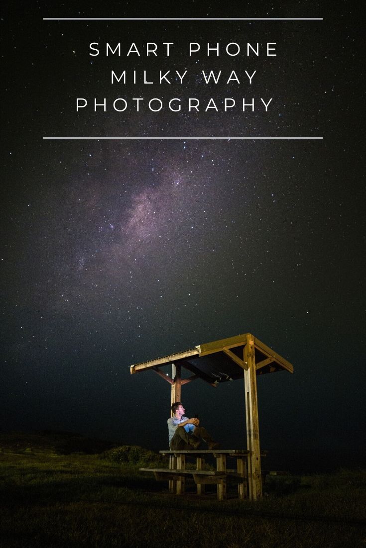 a man sitting on top of a wooden bench under a night sky filled with stars