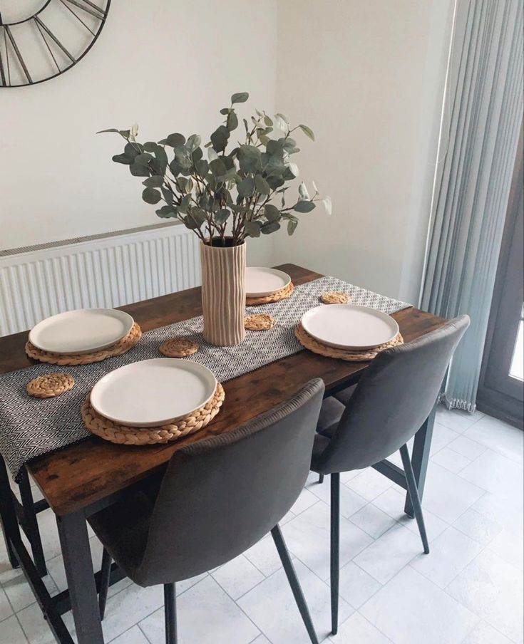 a dining room table with plates and flowers in a vase on the top, along with other place settings