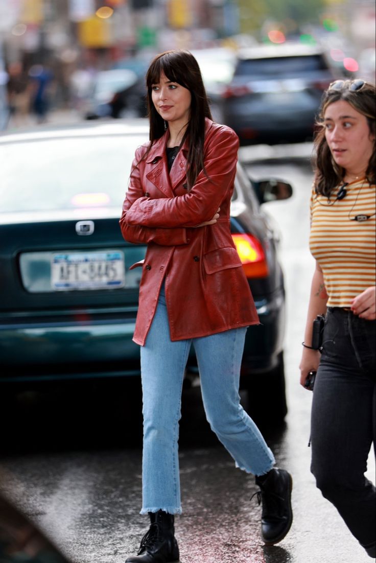 two women walking down the street in the rain, one is wearing a red leather jacket