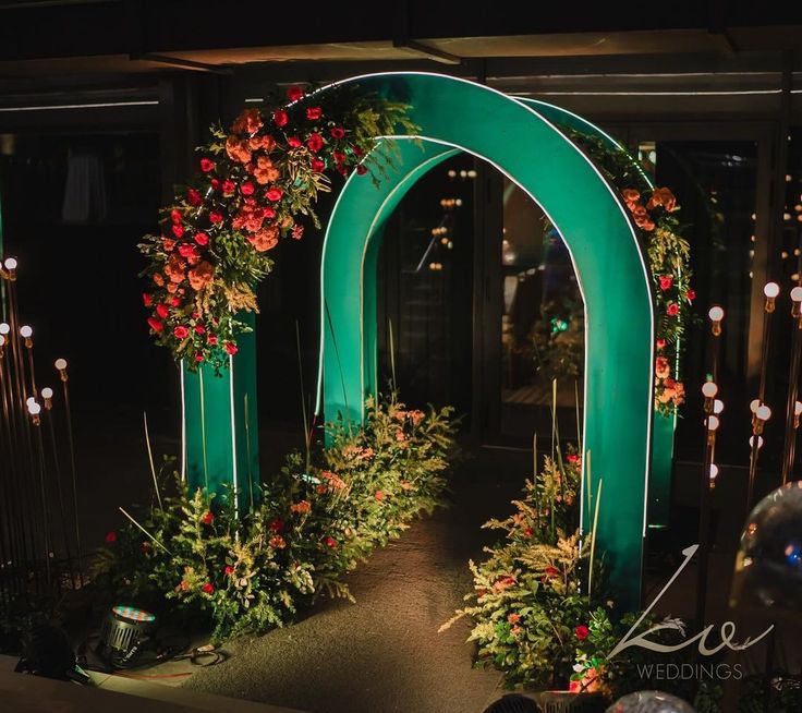 a green arch decorated with red flowers and greenery